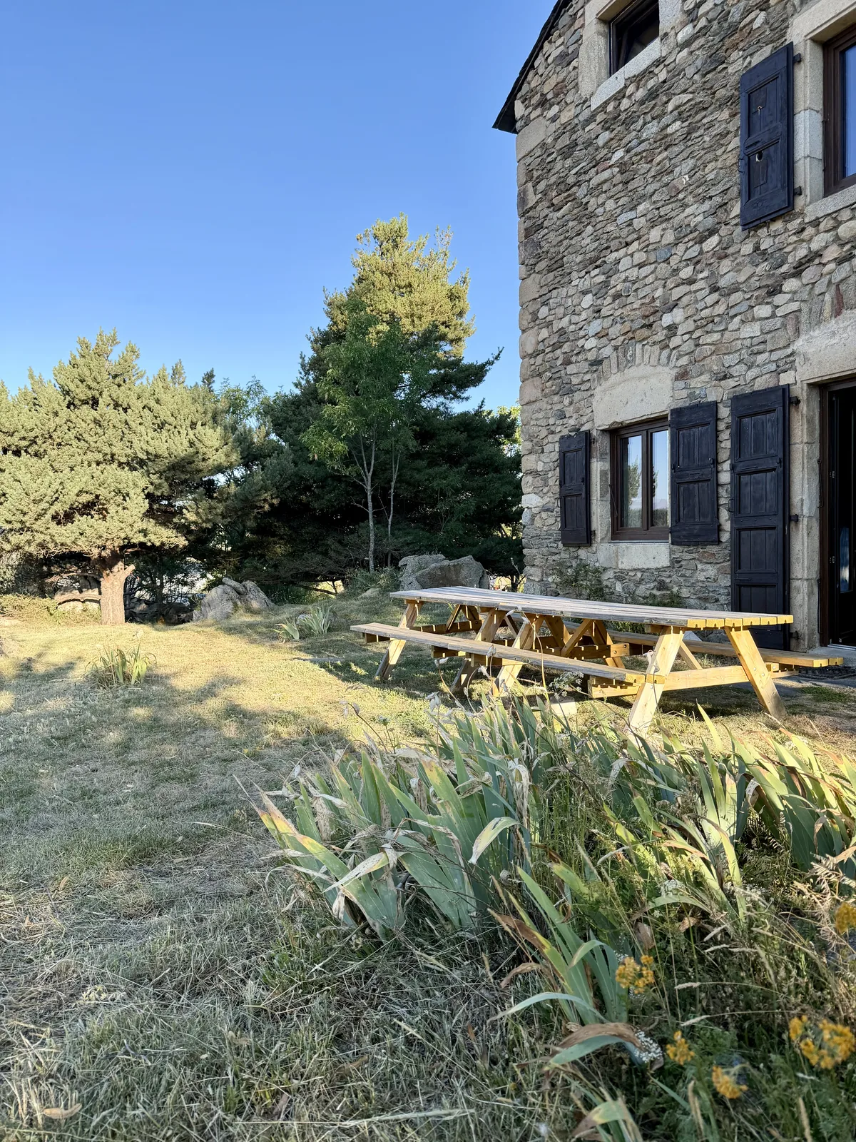 Le jardin de Maison Aline et sa grande table en bois, le long de la façade en pierre